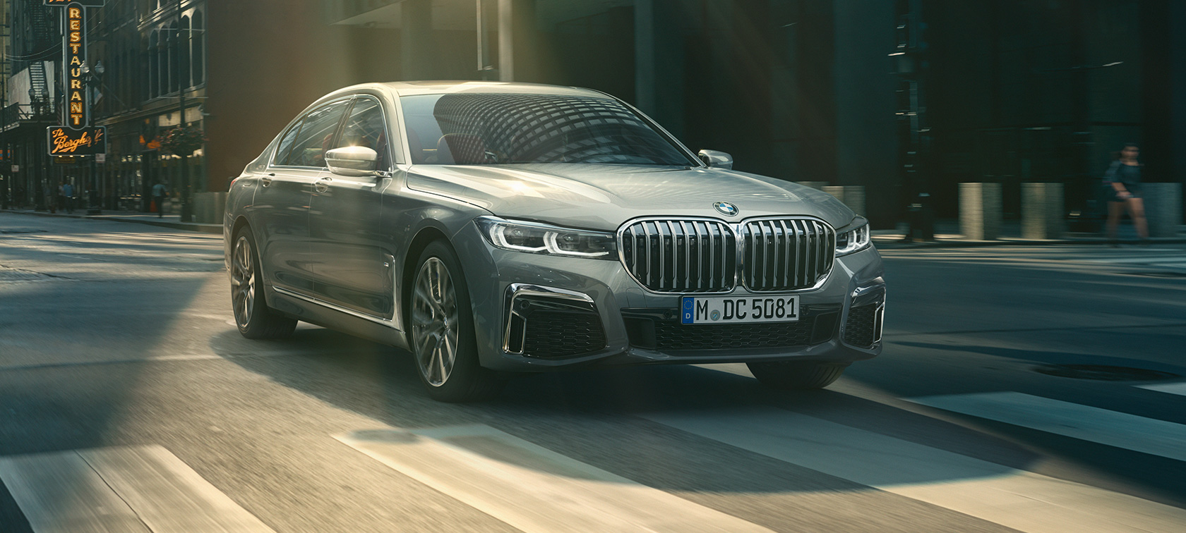 BMW 7 Series Sedan G11 G12 2019 Bernina Grey Amber Effect three-quarter front view driving through urban setting