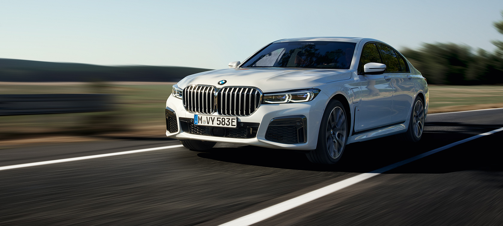 BMW 745e Sedan plug-in hybrid G11 G12 Mineral White metallic three-quarter front view driving on country road